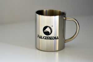 Ein Kaffeebecher aus Metall mit eingraviertem Logo von FALKEmedia.