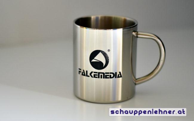 Ein Kaffeebecher aus Metall mit eingraviertem Logo von FALKEmedia.